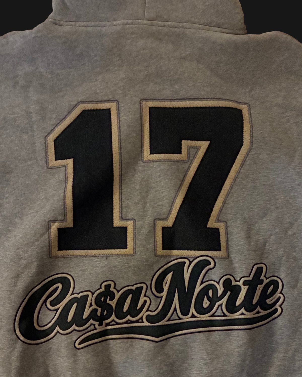 Close-up of the 17 and Ca$a Norte script graphic on the back of the heather gray hoodie